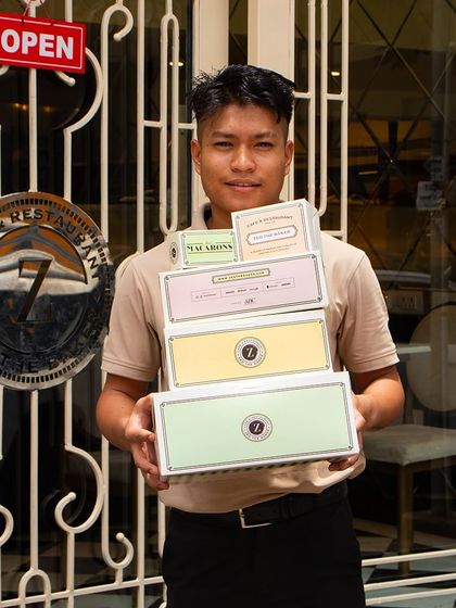 I'm proud of our beautiful, French-inspired packaging. Here, one of my team members holds a stack of our takeaway boxes, ready to bring a taste of Zed The Baker to your home.