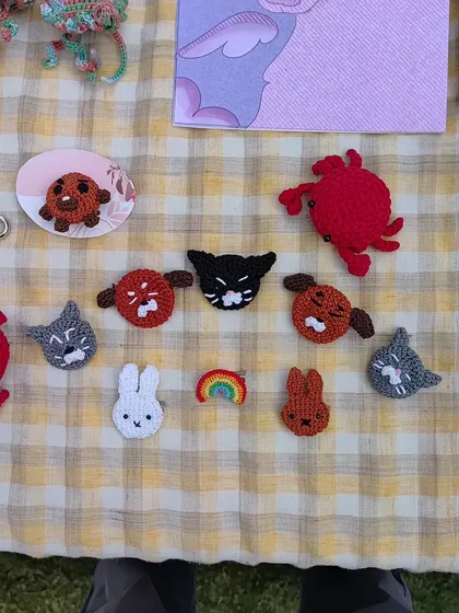 A close-up of some of my handmade pins on my market table. This little group includes a black cat, a gray cat, a white bunny, and a tiny rainbow, all stitched with lots of care. Each one is a perfect little piece of flair for a jacket or backpack.