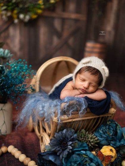 A classic newborn pose, with the baby resting his head on his hands in a rustic pram, surrounded by beautiful blue florals.