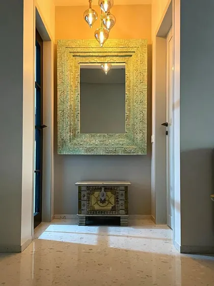 This symmetrical view highlights a curated moment in the Bohemian home. The warm pendant lighting enhances the intricate details of the mirror and chest, creating an inviting and artistic focal point.