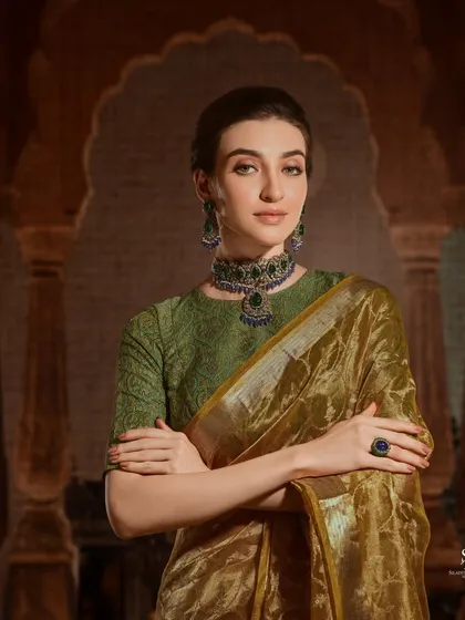 A model in an elegant olive green organza saree, paired with a stunning emerald and sapphire choker. The regal setting and confident pose create a look of pure sophistication for this jewellery campaign.