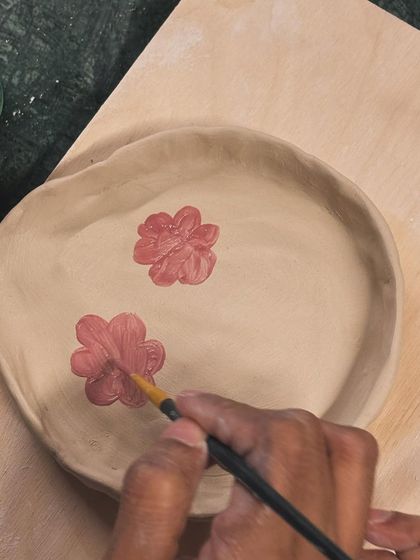Adding the finishing touches. A student paints delicate pink flowers onto a hand-built plate, a process that is both meditative and deeply personal.