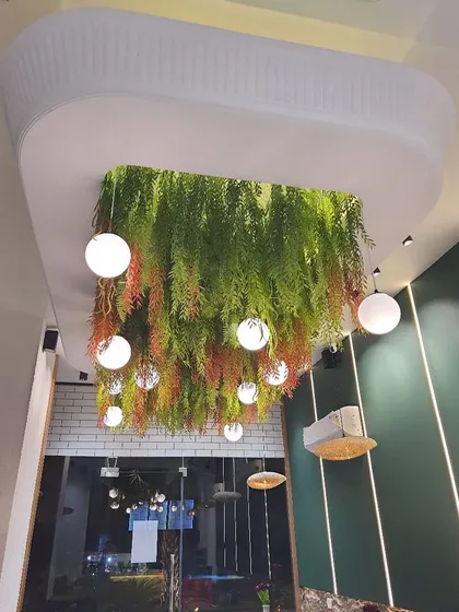 We designed this stunning ceiling installation for a cafe, featuring cascading artificial ferns and integrated globe lighting. It creates a warm, inviting canopy of green that makes the space feel unique and cozy.