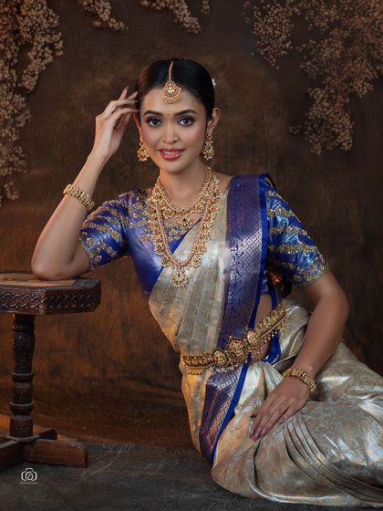 A beautiful portrait of a model in a traditional South Indian saree, seated beside a carved wooden table. The composition and lighting create a look of quiet elegance and grace.