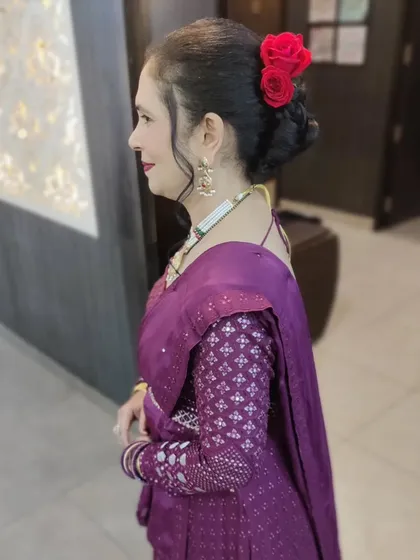 A side profile showcasing an elegant hair bun adorned with red roses. This hairstyle is paired with subtle makeup, making it a perfect look for a sophisticated evening party.