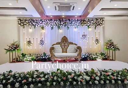 A grand and elegant engagement stage featuring a white floral header, a draped backdrop with candle-like lights, and a traditional royal sofa.