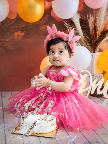 This little girl is covered in cake and happiness during her first birthday smash, a perfectly messy and joyful moment.