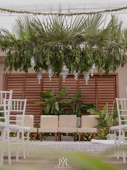 A closer look at the stage, where lush palm leaves and hanging silver lanterns create a tropical yet elegant feel against a wooden slat backdrop.