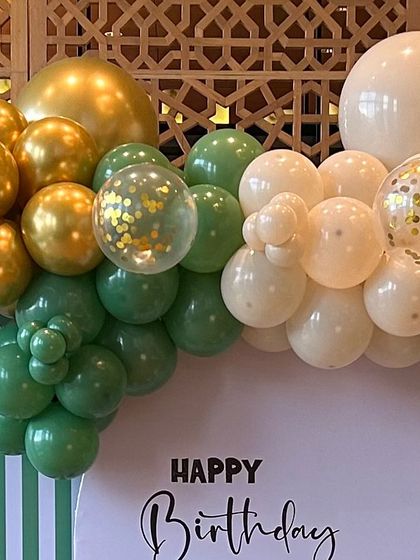A beautiful balloon garland in shades of green, white, and gold. The addition of clear confetti balloons adds a touch of sparkle to this elegant arrangement.