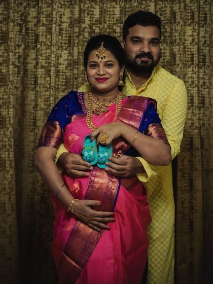 A traditional maternity shoot celebrating the family's culture. The couple holds up tiny baby shoes, a sweet symbol of the new life they are about to welcome.