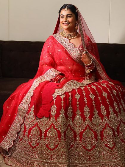 A full-length shot of a bride seated, showcasing her magnificent red lehenga and complementary makeup.