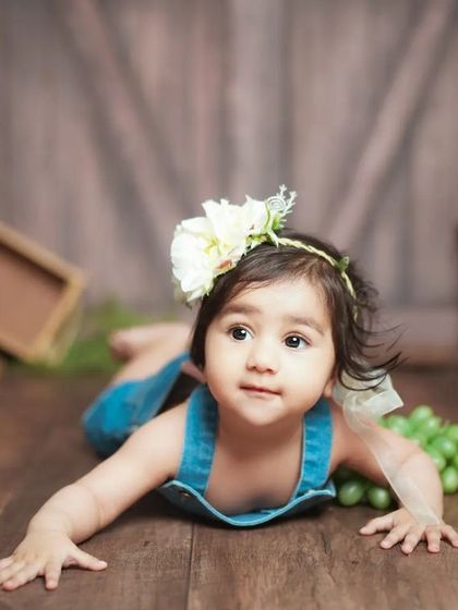 A rustic studio setup with a wooden floor and barn-door backdrop. This little girl's denim overalls complete the charming, vintage look.