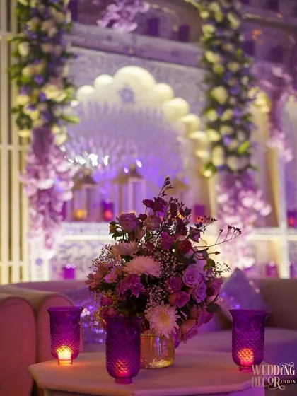 A close-up of a floral arrangement set against the ornate, lavender-lit backdrop. The soft focus on the background highlights the beauty of the flowers and the romantic candle lighting.