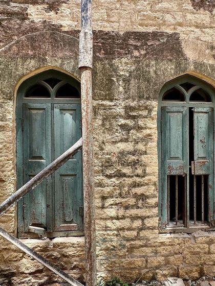 The weathered exterior of the school before restoration. The aged stone and faded green shutters show the building's state of disrepair, providing a "before" snapshot of our conservation work.
