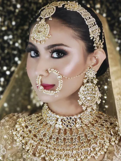 A close-up of a heavy, champagne-gold bridal set with intricate details and pearl accents. The matching nath and large earrings complete this stunning look.