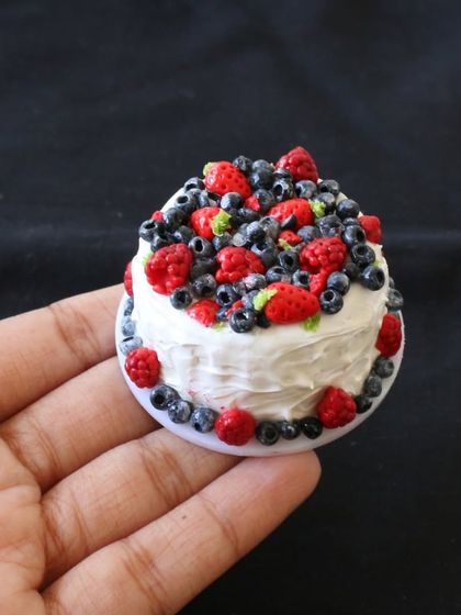 A miniature berry chantilly cake, topped with fresh-looking strawberries and blueberries.