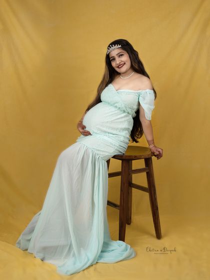 A royal pose on a stool. This mom-to-be wears a tiara and a lovely mint-colored gown, looking serene and happy against a yellow backdrop.