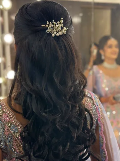 A bride's reflection in the mirror shows off her beautiful reception hairstyle. The half-updo with soft curls and a pearl accessory is a classic and elegant choice.