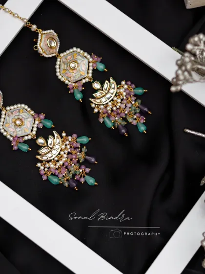 Framed by a clean white border against a dark, silky fabric, these traditional earrings are presented as a piece of art. This high-contrast composition makes the pastel Meenakari work and bead details pop.