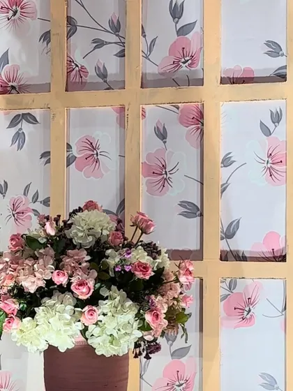 A beautiful floral arrangement set against a custom printed backdrop. The soft pink and white flowers complement the delicate floral pattern of the background panel, perfect for a Mehendi.