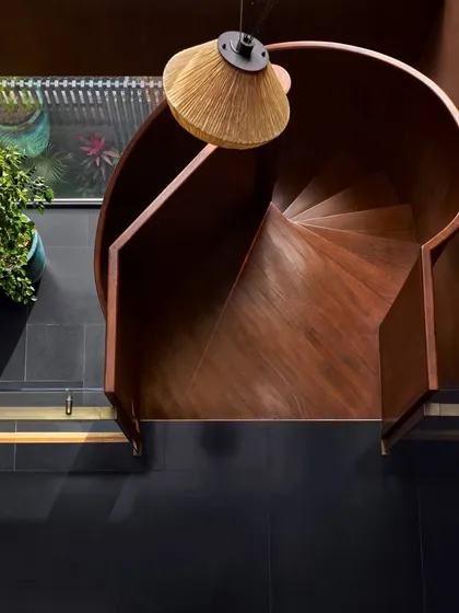 The blackened steel spiral staircase at the Baid Residence, seen from above. The design is both functional and sculptural, with an Oorjaa light fixture adding a touch of handcrafted warmth against the industrial metal.