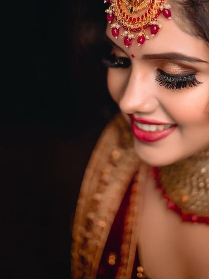 A beautiful close-up focusing on the bride's happy smile and stunning eye makeup. The dark background makes her features and jewellery pop.