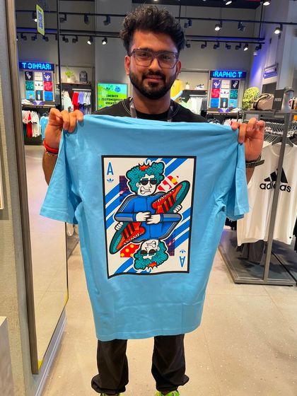 A customer showing off his new light blue Adidas tee with a custom playing card design featuring a cool, skeletal character.