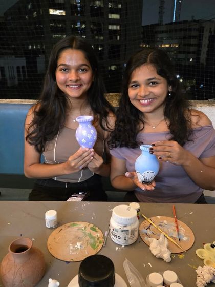 Two friends proudly display their beautifully painted vases. The intricate floral designs show the wonderful results of our pottery painting sessions.