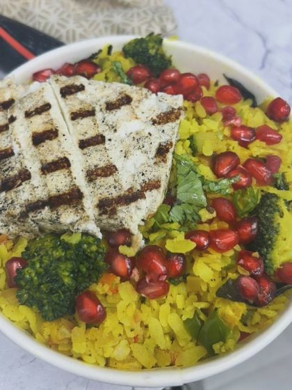 A bowl of colorful poha topped with grilled paneer and pomegranate seeds. A creative and delicious client meal.