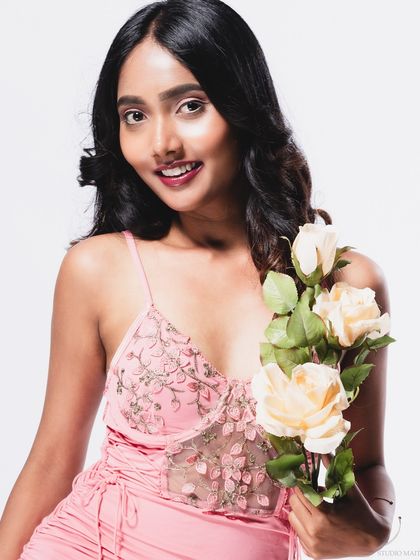 A smiling portrait of a model in a pink dress, holding roses.