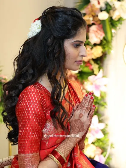 A moment of prayer during a pre-wedding ceremony. The bride's hairstyle is a half-up, half-down look with soft curls, adorned with a simple gajra for an elegant touch.