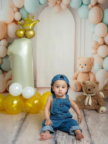 Posing like a pro, this little one sits confidently amidst his first birthday decorations, including a large "1" balloon and a golden crown.