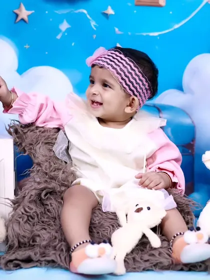 A one-year-old baby girl celebrating her birthday with teddy bears and a sky-themed backdrop.