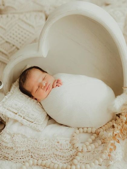 A newborn swaddled in white, sleeping inside a beautiful heart-shaped bowl for a simple and love-filled portrait.