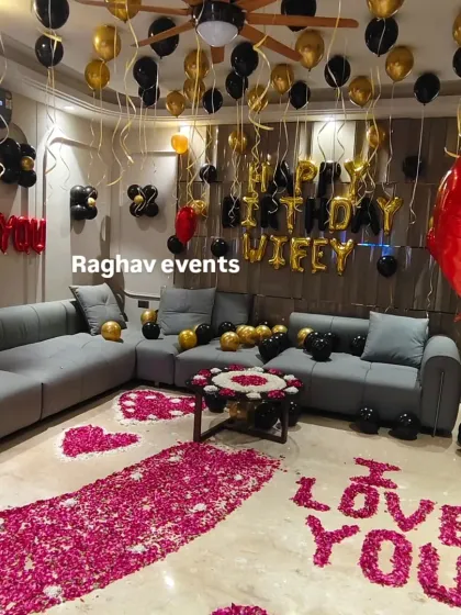 This is an example of a complete living room transformation for a romantic celebration. The setup includes "HAPPY BIRTHDAY WIFEY" and "I LOVE YOU" messages, a dense pathway of rose petals, and a coordinated black and gold balloon theme for a luxurious feel.
