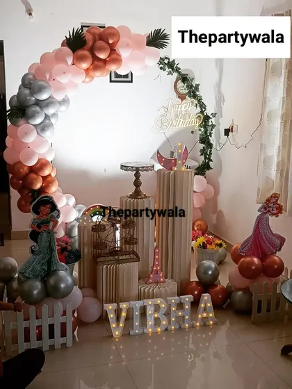 A cozy at-home princess party setup. The rose gold, pink, and silver balloon arch with character cutouts transforms the living room into a magical kingdom.