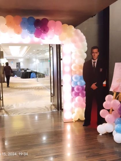 An entrance arch with a light-up frame and pastel balloons, with security personnel present for a large event.