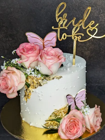 A chic and floral cake for a bride-to-be. This chocolate hazelnut mousse cake is decorated with fresh pink roses, butterflies, and gold leaf for an elegant touch.