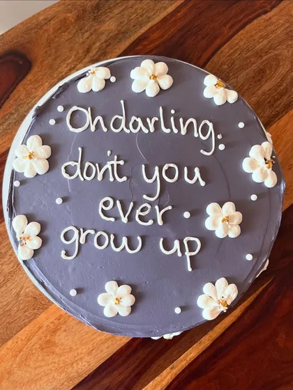 A cake with a sweet message from the Taylor Swift song "Never Grow Up." The purple buttercream is decorated with simple white piped flowers.