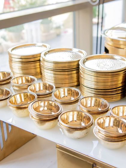 Stacks of shining, gold-toned plates and bowls, ready for guests. I ensure that even the basic elements of the dining experience reflect a standard of luxury and attention to detail.