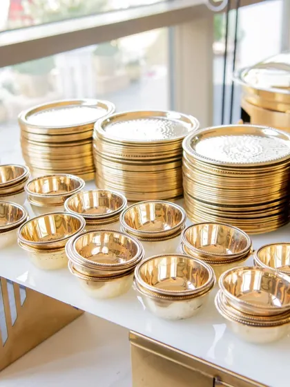 Stacks of shining, gold-toned plates and bowls, ready for guests. I ensure that even the basic elements of the dining experience reflect a standard of luxury and attention to detail.