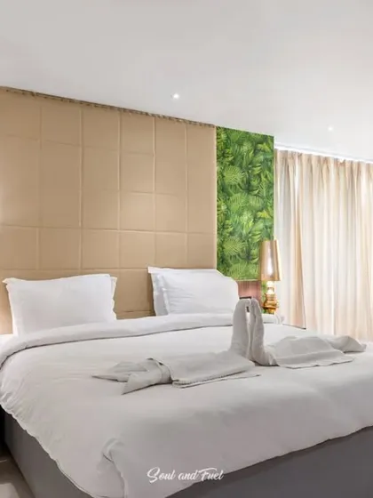 A hotel room at Hotel Niranjana, Bodh Gaya, featuring a vibrant green-leaf accent wall. The crisp white bedding and modern decor create a fresh and welcoming space for guests.