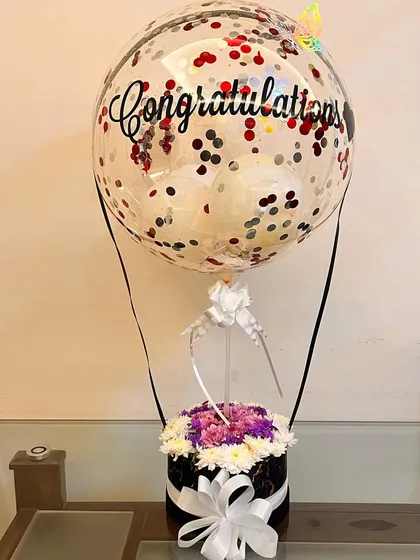 Our hot air balloon arrangements are perfect for any celebration. This one, customized with a 'Congratulations' message, features a mix of chrysanthemums and a balloon filled with red and silver confetti.