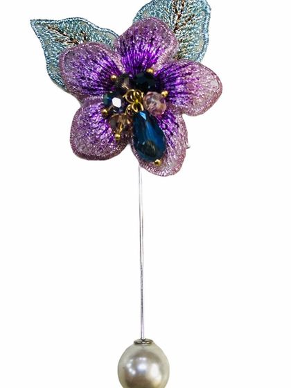 A beautiful lapel pin featuring a purple embroidered flower with blue bead accents and a classic pearl drop. The vibrant color makes it a standout accessory.