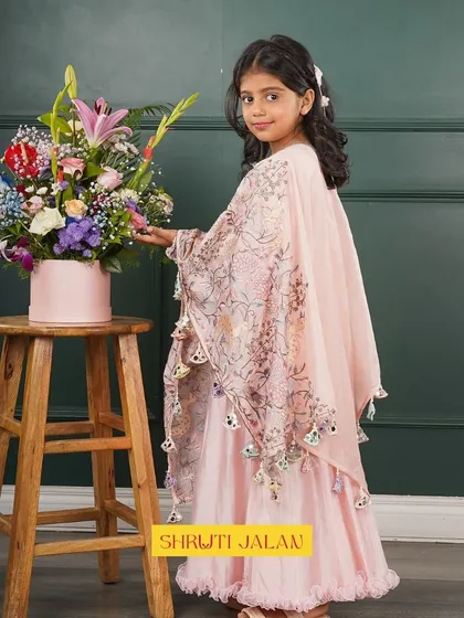 This little girl looks so elegant in a blush pink cape gown, posing next to a bouquet of flowers. The outfit is perfect for a wedding or formal party.
