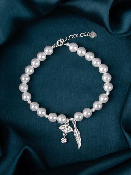 A pearl bracelet with silver evil eye and feather charms.