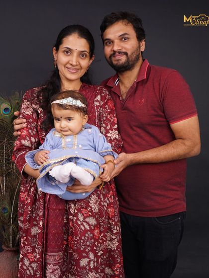 A beautiful studio family portrait. The parents are holding their baby girl, who is dressed in a lovely traditional-style outfit, creating a timeless and elegant family photo.