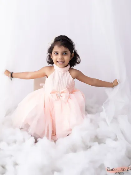 A beautiful portrait of a little girl sitting among the "clouds." The soft pink dress and dreamy white background create a magical, storybook feel.