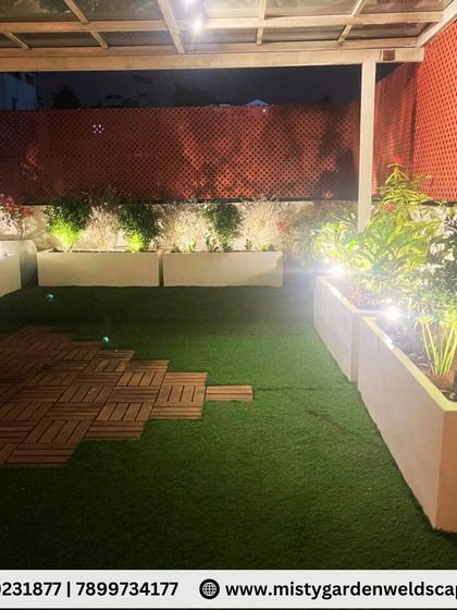 A beautiful night view of a terrace makeover in Banashankari. We used a glass pergola, artificial grass, and FRP planters with integrated lighting to create a peaceful and elegant family gathering space.