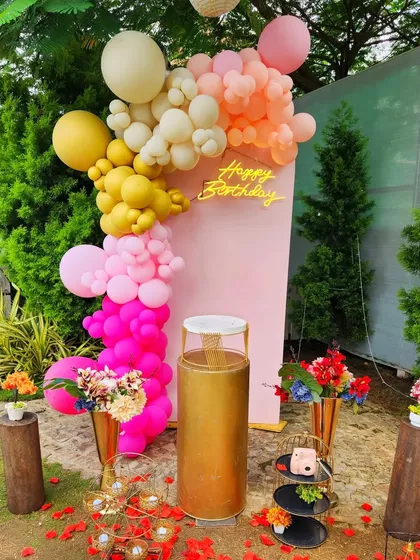A vibrant and colorful birthday backdrop. This setup uses a bright pink panel and a multi-colored balloon garland in shades of pink, yellow, and orange, creating a joyful and energetic photo spot.